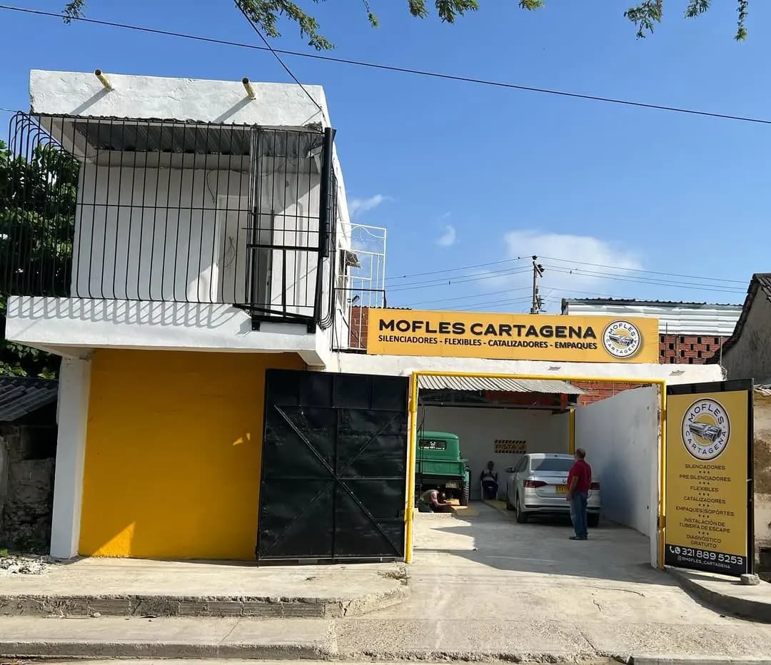 Fachada del taller Mofles Cartagena: local amarillo con puerta de enrollable negra y aviso distintivo en el barrio Torices
